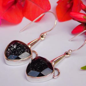 May include: A pair of silver earrings with black heart-shaped stones. The stones have a unique, sparkly, and textured appearance.