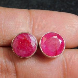 May include: A pair of silver earrings with round, red ruby gemstones.