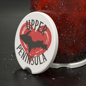 May include: White ceramic coaster with a red heart featuring a black silhouette of the Upper Peninsula of Michigan. The text "Upper Peninsula" is written around the heart.