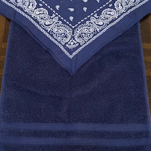 May include: A navy blue towel with a matching navy blue bandana. The bandana is folded and placed on top of the towel. The bandana has a white paisley pattern.