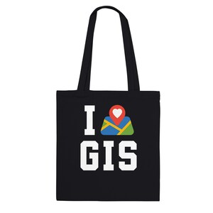 以下が含まれることがあります： 「I GIS」の白い文字が入った黒いトートバッグ。 「I」の後には、赤いハートのピンが付いた地図アイコンがあります。 バッグには2つの黒いハンドルが付いています。