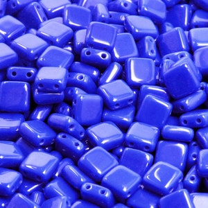 May include: A close-up image of a pile of small, square, cobalt blue glass beads. The beads have a glossy finish and are perfect for jewelry making.