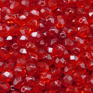 Può includere: Un'immagine ravvicinata di una grande quantità di perline di vetro rosso. Le perline sono sfaccettate e hanno una finitura lucida e traslucida.
