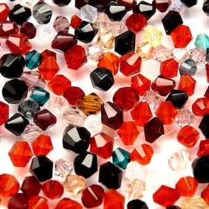 Könnte beinhalten: Eine Auswahl an bunten Glasperlen in verschiedenen Formen und Größen. Die Perlen sind hauptsächlich rot, schwarz und klar, mit einigen grünen und goldenen Akzenten. Die Perlen sind in einem zufälligen Muster auf einem weißen Hintergrund angeordnet.