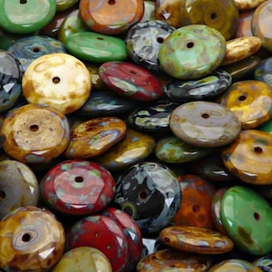 Può includere: Una collezione di perline rotonde in ceramica colorate con un foro al centro. Le perline presentano una varietà di motivi e colori, tra cui marrone, verde, blu e rosso.