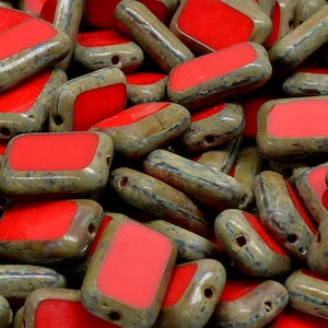 Op de afbeelding: Een stapel rechthoekige glazen kralen in rood en groen. De kralen hebben een gevlekte groene buitenkant en een gladde rode binnenkant.