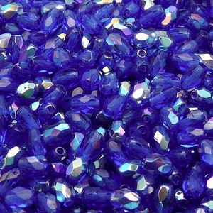 May include: A close-up view of a pile of iridescent blue glass beads. The beads are faceted and have a teardrop shape.