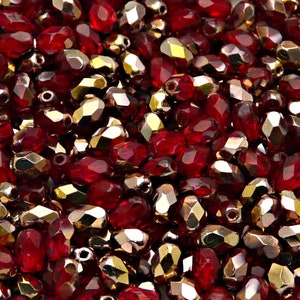 Può includere: Primo piano di un mucchio di perline di vetro rosse e dorate. Le perline sono sfaccettate e hanno una finitura lucida.