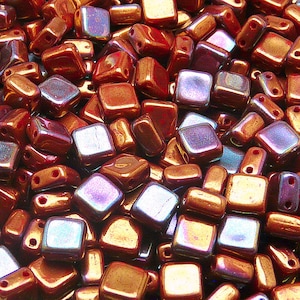 Può includere: Un grande mucchio di piccole perline quadrate di vetro iridescente. Le perline sono un mix di colori rame e viola.