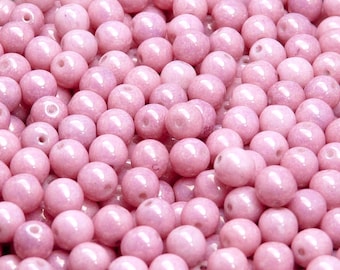 May include: A close-up of a pile of pink glass beads. The beads are round and have a smooth, shiny finish.
