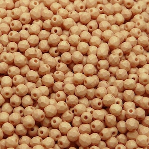 May include: A large quantity of small, peach-coloured, faceted glass beads. The beads are all the same size and shape, and they are arranged in a random pattern.