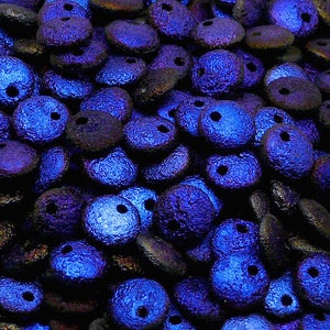 Può includere: Primo piano di un mucchio di perline di vetro blu iridescente con due fori ciascuna. Le perline hanno una superficie testurizzata e sono perfette per la creazione di gioielli.