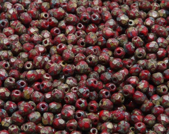 May include: A close-up view of a large quantity of red and brown faceted glass beads. The beads have a speckled, marbled appearance.
