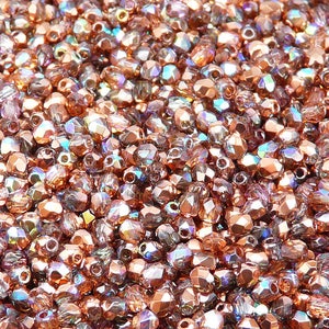 Può includere: Una vista ravvicinata di una grande quantità di piccole perline di vetro sfaccettate e iridescenti di colore rame. Le perline sono sparse casualmente, creando una superficie scintillante e testurizzata.