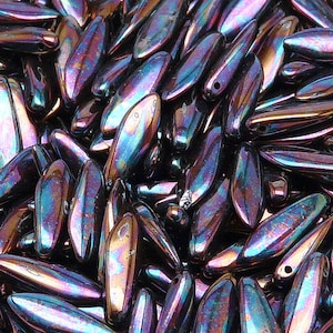 Könnte beinhalten: Ein großer Haufen irisierender lila und blauer Glasperlen. Die Perlen sind lang und schmal, mit einem spitzen Ende. Sie sind perfekt für die Schmuckherstellung oder andere Bastelprojekte.