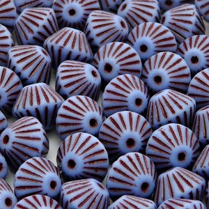 Puede incluir: Primer plano de un montón de cuentas de vidrio azul con un diseño radial de color púrpura oscuro. Las cuentas son facetadas y tienen un agujero en el centro.