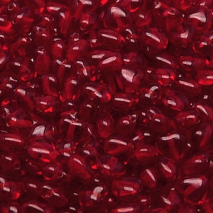 Pode incluir: Uma imagem em close-up mostra uma densa coleção de contas translúcidas em forma de gota. As contas são de um vermelho profundo e rico, com um acabamento brilhante que reflete a luz. As contas são provavelmente usadas para fazer joias ou artesanato.