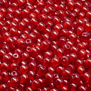 Puede incluir: Una imagen de primer plano de una gran cantidad de pequeñas cuentas de vidrio rojas. Las cuentas son redondas y tienen una ligera forma de lágrima.