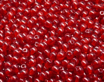 May include: A close-up image of a large quantity of small, red, glass beads. The beads are round and have a slight teardrop shape.
