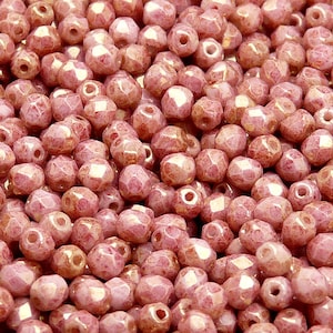 May include: A close-up view of a pile of small, pink, faceted glass beads. The beads have a slightly iridescent finish and a textured surface.