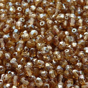 May include: A close-up image of a pile of amber glass beads. The beads are faceted and have a shimmery finish.