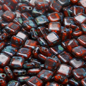 May include: A close-up of a pile of small, square, red and blue glass beads. The beads have a speckled, iridescent finish.