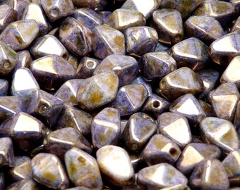 Könnte beinhalten: Nahaufnahme eines Haufens irisierender lila und goldener Glasperlen. Die Perlen sind facettiert und haben eine leicht unregelmäßige Form.