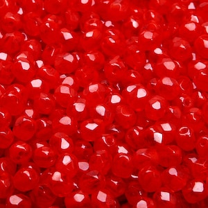 May include: A close-up image of a pile of small, red, faceted glass beads. The beads are shiny and translucent, and they are all about the same size.