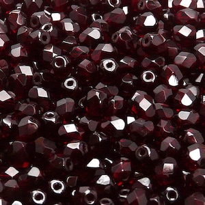 Puede incluir: Primer plano de una gran cantidad de cuentas de vidrio facetadas de color rojo oscuro. Las cuentas son pequeñas y tienen una superficie brillante y reflectante.