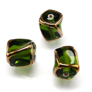 May include: Three green glass beads with gold trim. The beads are square shaped with rounded edges and have a hole in the center.