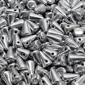 Könnte beinhalten: Ein großer Haufen silberfarbener, kegelförmiger Perlen mit einem Loch oben. Die Perlen sind glänzend und haben eine metallische Oberfläche.