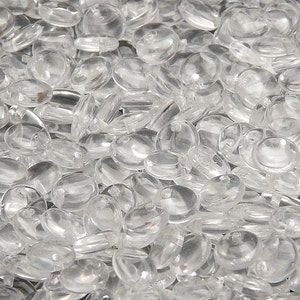 May include: A close-up shot of a pile of clear, oval-shaped beads. The beads are transparent and appear to be made of glass or a similar material. They are scattered randomly, creating a textured surface.