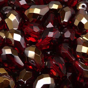 May include: A close-up of a pile of red and gold faceted glass beads. The beads are all different shapes and sizes, and they are arranged in a random pattern.
