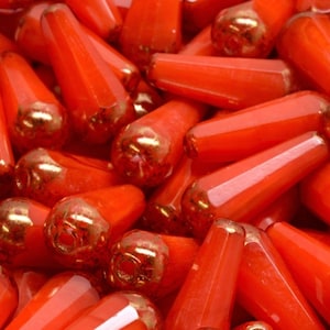 Puede incluir: Un montón de cuentas de vidrio naranja con detalles dorados. Las cuentas tienen forma de lágrima y un acabado brillante.