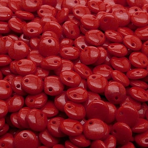 May include: A close-up shot displays a pile of glossy, red, disc-shaped beads. Each bead has a small hole for stringing. The beads are smooth and reflect light, creating a vibrant and eye-catching display. These beads are suitable for jewelry making and crafting.