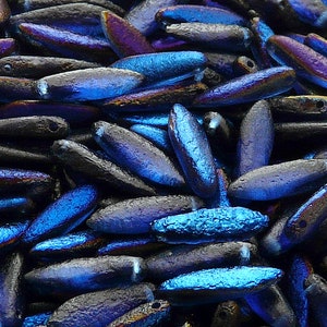May include: A close-up of a pile of iridescent blue and black glass beads. The beads are oval shaped and have a textured surface.