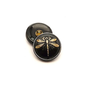 May include: Two black buttons with a gold dragonfly design. The buttons are round and have a shiny finish.