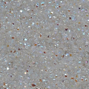 May include: A close-up of a large quantity of small, clear iridescent glass beads. The beads are scattered randomly and have a variety of shapes and sizes.