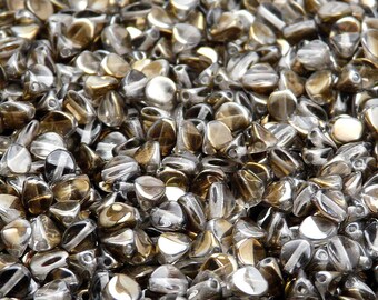 Könnte beinhalten: Nahaufnahme eines Haufens kleiner, klarer Glasperlen mit goldfarbenem, irisierendem Finish. Die Perlen sind tropfenförmig und haben eine spitze Spitze.
