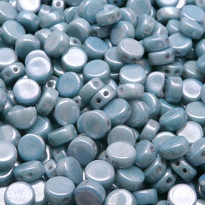 Könnte beinhalten: Ein großer Haufen hellblauer runder Glasperlen mit jeweils zwei Löchern. Die Perlen haben eine leicht irisierende Oberfläche.