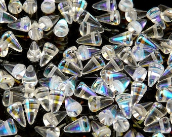 May include: A collection of clear, cone-shaped glass beads with iridescent, rainbow-like color reflections. Each bead has a rounded top and a band near the top. The beads are scattered on a dark surface.