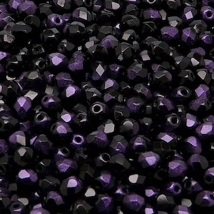 May include: A close-up view of a large quantity of dark purple glass beads. The beads are faceted and have a shiny finish.