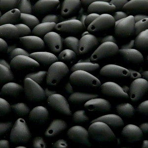 May include: A close-up of a pile of black glass beads in a teardrop shape. The beads have a matte finish.