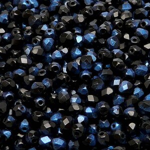 May include: A close-up image of a large quantity of dark blue and black faceted glass beads. The beads have a metallic sheen and are scattered randomly.