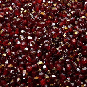 Peut inclure: Gros plan d'un tas de petites perles de verre rouges facettées. Les perles ont une finition brillante et irisée.