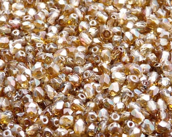 May include: A close-up image of a large quantity of small, faceted, iridescent glass beads in a light amber colour.