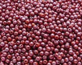 May include: A large quantity of small, round, burgundy-colored beads. The beads have a slight iridescent sheen.
