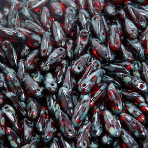 May include: A large pile of dark red and blue glass beads with white speckles. The beads are shaped like teardrops and have a glossy finish.