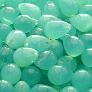 May include: A close-up of a group of teal blue glass teardrop beads. The beads are smooth and shiny, and they are arranged in a random pattern.