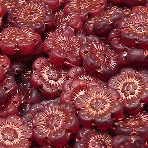 Op de afbeelding: Een close-up van een stapel rode glazen bloemen kralen. De kralen hebben een koperen metallic afwerking en een reliëf bloemendesign.